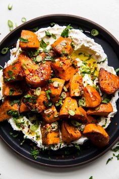 a black plate topped with mashed sweet potatoes and sour cream sauce, garnished with chopped green onions