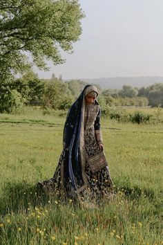 a woman standing in the middle of a field wearing a sari and head scarf