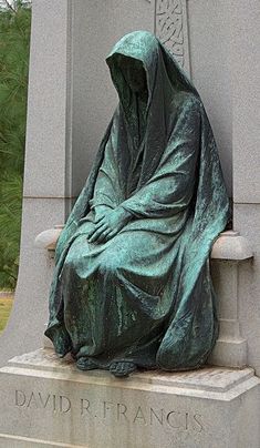 a statue of a woman wrapped in a blanket sitting on a stone bench next to a tree