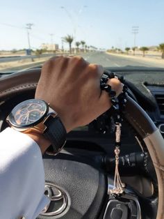 a person wearing a wrist watch while sitting in a car with a steering wheel on the dashboard