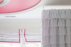 a white curtain with pink trim hanging from the ceiling in front of a large window