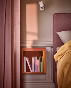 a book shelf with books on top of it next to a pink headboard in a bedroom