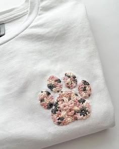 a white t - shirt with pink and black flowers on the front, embroidered onto it