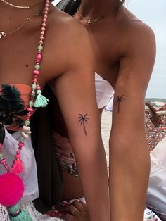 two women with tattoos on their arms and legs sitting next to each other at the beach