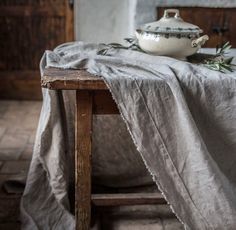 an old wooden table with a cloth draped over it and a white bowl on top