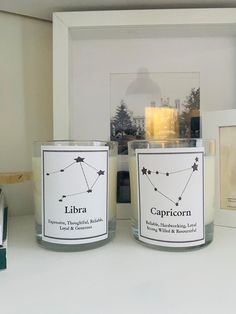 two candles sitting next to each other on a counter in front of a picture frame