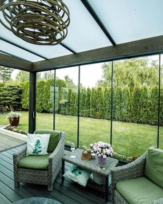 an enclosed patio with wicker furniture and green cushions on the wooden decking area