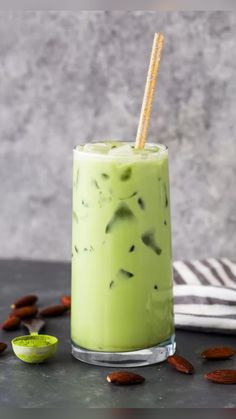 a green smoothie in a glass with a straw and some almonds around it