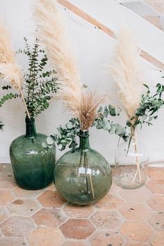 three green vases filled with plants and greenery