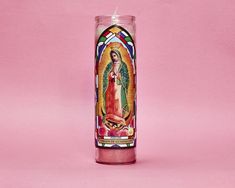 a candle with an image of the virgin mary on it in front of a pink background