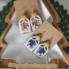 two pairs of earrings are on display in a wooden box with green leaves and snowflakes