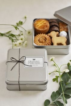 two tins filled with pastries on top of a white table next to flowers