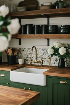 a kitchen with green cabinets and white flowers on the counter top, along with wooden shelves