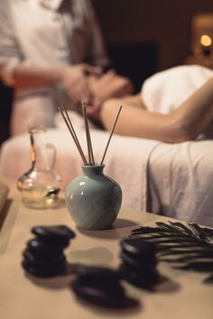 a couple getting massages in the background with candles and rocks on the table next to them