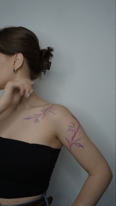 a woman with a tattoo on her shoulder pointing to the side while standing in front of a wall