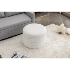 a white round ottoman sitting on top of a shaggy rug next to a gray couch