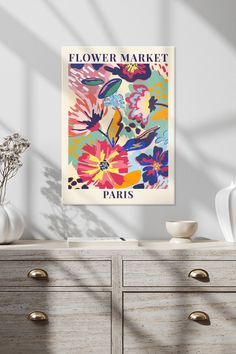 a flower market poster hangs on the wall next to a dresser with drawers and vases