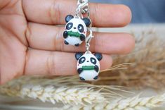 a person holding two panda bears in their hands on a chain with some ears hanging from it