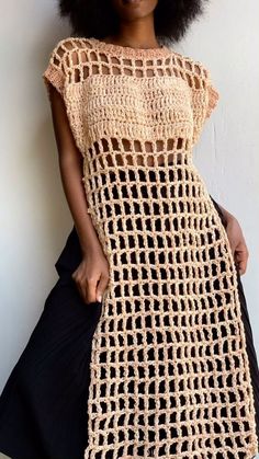 a woman standing in front of a wall wearing a crocheted dress