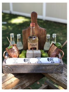 a wooden tray with bottles and glasses in it sitting on top of a picnic table