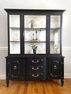 a black china cabinet sitting on top of a hard wood floor