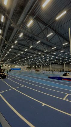 an indoor track with lights on the ceiling and blue running tracks in front of it