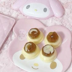 four small desserts on a pink plate next to a hello kitty mask shaped case