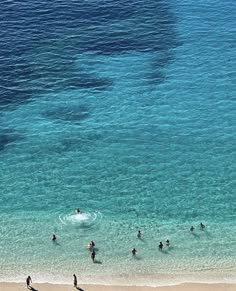 several people are swimming in the ocean on a beach with clear blue water and one person is holding a surfboard