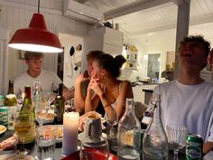 a group of people sitting at a table with bottles and glasses on it, all looking up