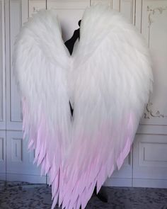 a large white and pink angel wings on a mannequin stand in front of a wall