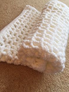 a white crocheted blanket laying on top of a floor next to a brown carpet