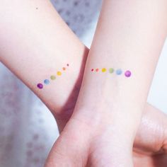 two people with matching tattoos on their arms holding each other's wrists, both showing different colored dots