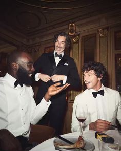 three men in tuxedos sitting at a dinner table