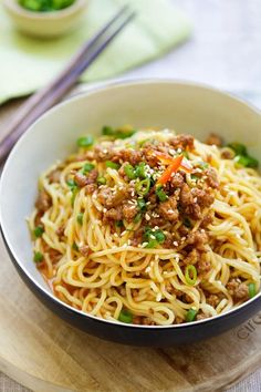 a white bowl filled with noodles and meat on top of a wooden table next to chopsticks