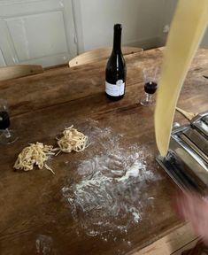 a person is making pasta on a wooden table with wine bottles and utensils