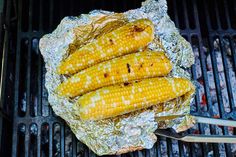 grilled corn on the cob with tongs sitting on foil wrapped in tinfoil