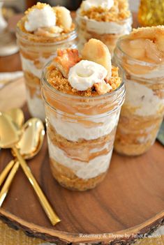 four desserts in glass jars on a wooden tray with spoons and goldware