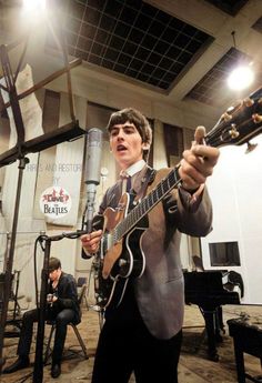 a man in a suit and tie holding a guitar while standing next to a microphone