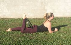 a woman laying on the grass with her leg up in the air while holding a tennis racquet