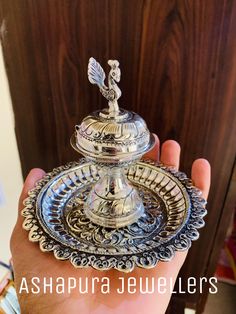 a person is holding a silver plate with a bird on it and the words ashpurra jewellers above it