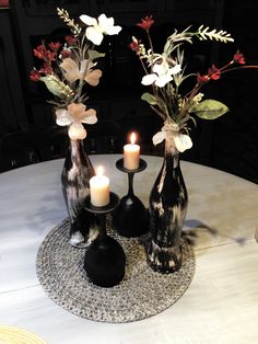 three black vases with flowers and candles on a round white tableclothed placemat