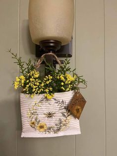 a hanging basket filled with yellow flowers on a wall next to a light fixture and lamp