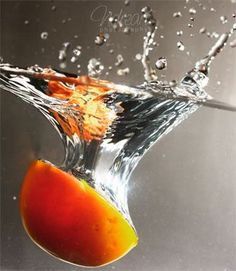 an orange falling into the water with splashing from it's top and bottom