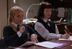 two women sitting at a table with notebooks and papers