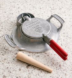 an old tea kettle with a red handle next to a small wooden stick on the ground