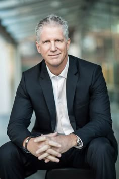 a man in a suit sitting on a chair with his arms crossed and looking at the camera