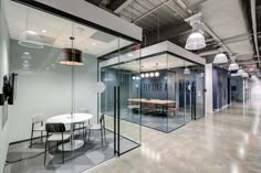 an office with glass walls and tables in the center, along with hanging lights on the ceiling