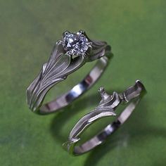 two silver rings with flowers on them sitting on a green surface, one has a diamond in the center