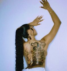 a woman with tattoos on her back standing in front of a wall and reaching up into the air