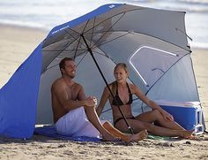 a man and woman sitting under an umbrella on the beach